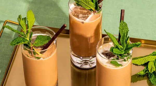 Trois mocktails rafraîchissants à la menthe et au chocolat, servis dans des verres hauts avec de la glace et des pailles foncées.