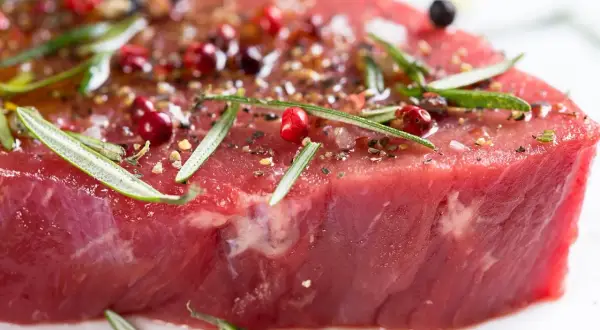Un morceau de bœuf cru, assaisonné de poivre rose, de romarin et d'épices, promettant le meilleur bœuf du monde.