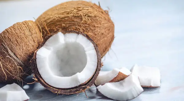 Noix de coco entières et coupées, révélant leur chair blanche et leur peau fibreuse. Des morceaux de noix de coco sont dispersés autour.