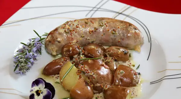 Une andouillette sauce moutarde, accompagnée de pommes de terre grenaille et d'une touche de romarin et de pensée.