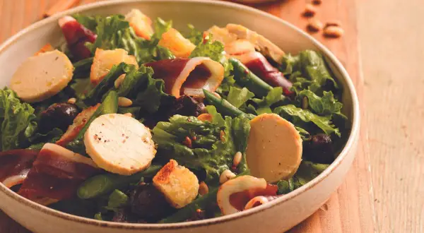 Salade périgourdine : foie gras, magret fumé, asperges vertes, croûtons et olives noires dans un bol.