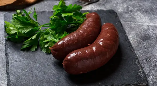 Deux boudins rouges antillais, brillants et appétissants, accompagnés de persil frais sur une ardoise sombre.