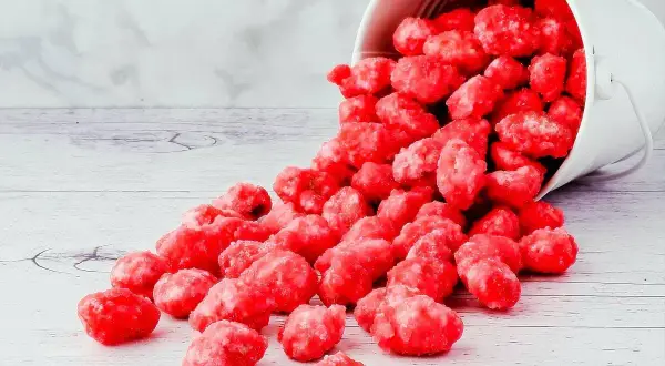 Un seau blanc renversé déverse des bonbons roses brillants, parfaits pour une recette praline rose.