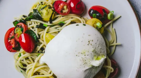 Un plat de pâtes avec une burrata crémeuse, des tomates cerises rouges et jaunes, et des herbes vertes.