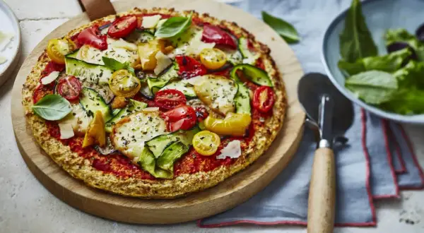 Délicieuse pizza aux légumes frais et fromage, sur une pâte sans gluten, servie sur une planche en bois.