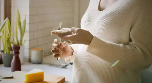 Une personne tartine une tranche de pain avec du fromage au lait cru. Un morceau de fromage est posé sur une planche à découper.