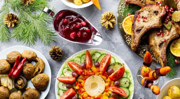 Une table dressée pour une entrée chaude festive : côtelettes de porc, légumes rôtis, salade colorée et sauce aux airelles.