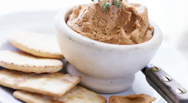 Un bol de pâté onctueux, garni de thym, servi avec des crackers. Un débat culinaire : foie gras vs pâté.
