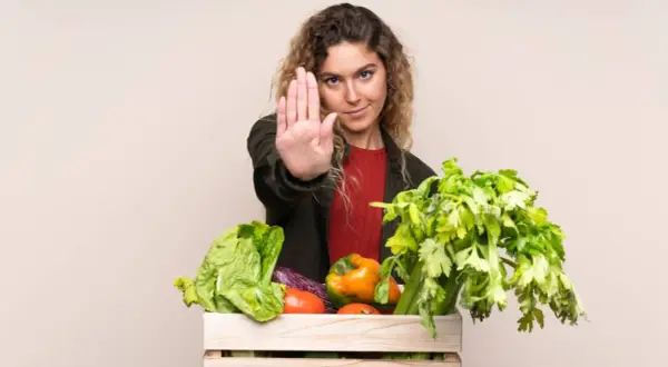 Femme faisant un geste d'arrêt devant une caisse de légumes frais, comme pour dire non aux légumes crus toxiques.