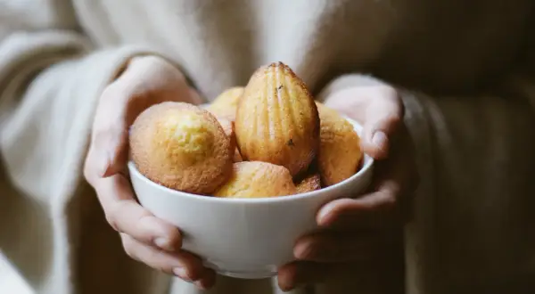 Mains tenant un bol de madeleines dorées, évoquant la madeleine de Proust recette.