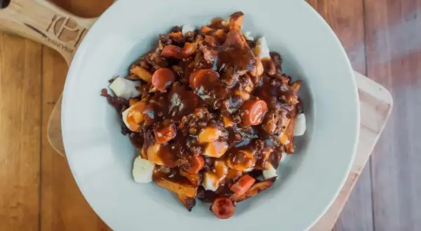 Une assiette généreuse de recette poutine québécoise, avec frites, fromage en grains, sauce brune et morceaux de saucisses.
