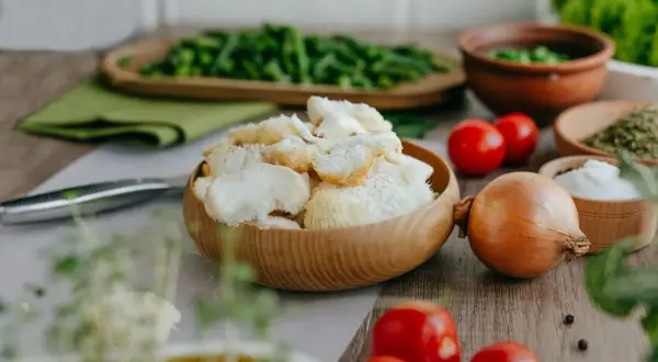 Un bol en bois rempli de champignon criniere de lion, prêt pour une recette savoureuse. Tomates, oignon et herbes l'accompagnent.
