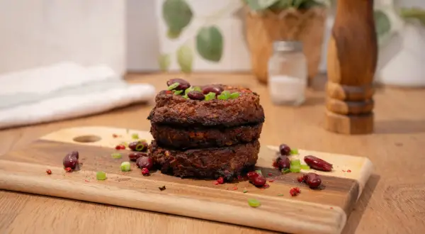 Trois galettes de haricot rouge empilées, garnies de haricots rouges et de ciboule. Épices et haricots rouges parsèment la planche à découper.