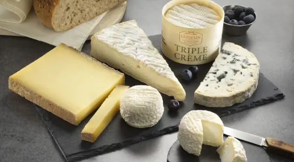 Plateau de fromages variés, dont un bleu et un triple crème, accompagnés de pain artisanal. Un délice pour les amateurs de fromage fort en goût.