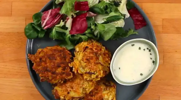 Trois croquettes de légumes dorées, accompagnées d'une salade fraîche et d'une sauce crémeuse.