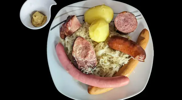 Assiette de choucroute garnie avec pommes de terre, saucisses et viandes, un petit ramequin de moutarde à côté. Un plat riche en saveurs et en vitamine C !
