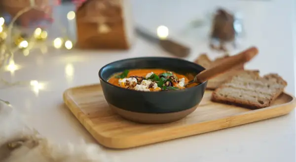 Un bol de soupe butternut tomate onctueuse, garnie de fromage frais et de noix, servi avec du pain grillé.