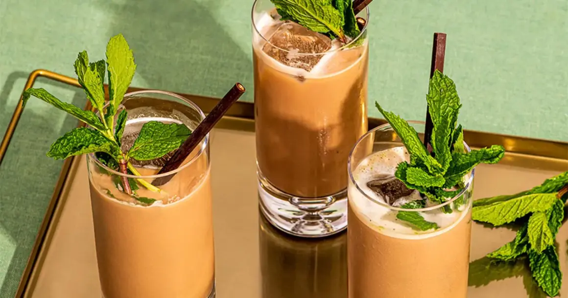 Trois mocktails rafraîchissants à la menthe et au chocolat, servis dans des verres hauts avec de la glace et des pailles foncées.