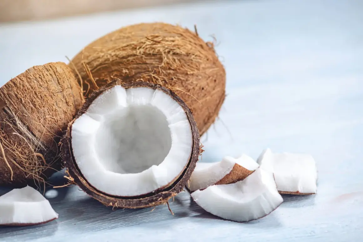 Noix de coco entières et coupées, révélant leur chair blanche et leur peau fibreuse. Des morceaux de noix de coco sont dispersés autour.