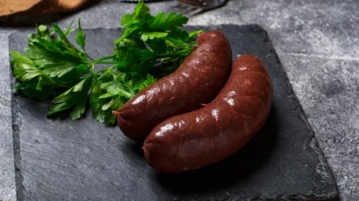 Deux boudins rouges antillais, brillants et appétissants, accompagnés de persil frais sur une ardoise sombre.