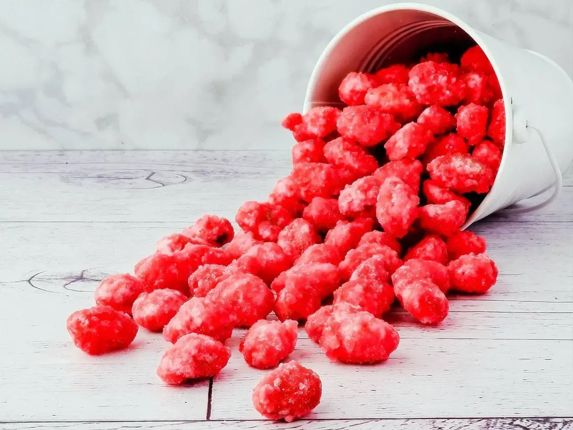 Un seau blanc renversé déverse des bonbons roses brillants, parfaits pour une recette praline rose.