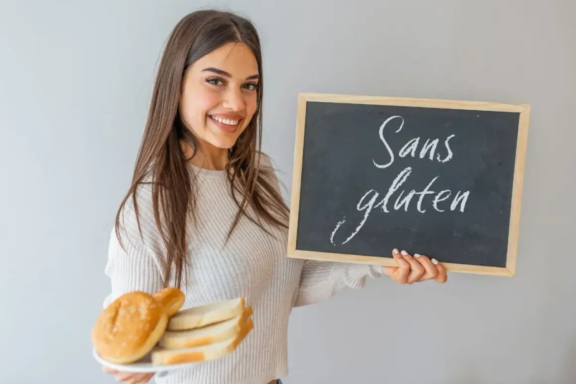 Une jeune femme souriante tient une assiette de pain et un tableau noir "Sans gluten". Elle montre ce qu'il faut manger en cas d'intolérance au gluten.