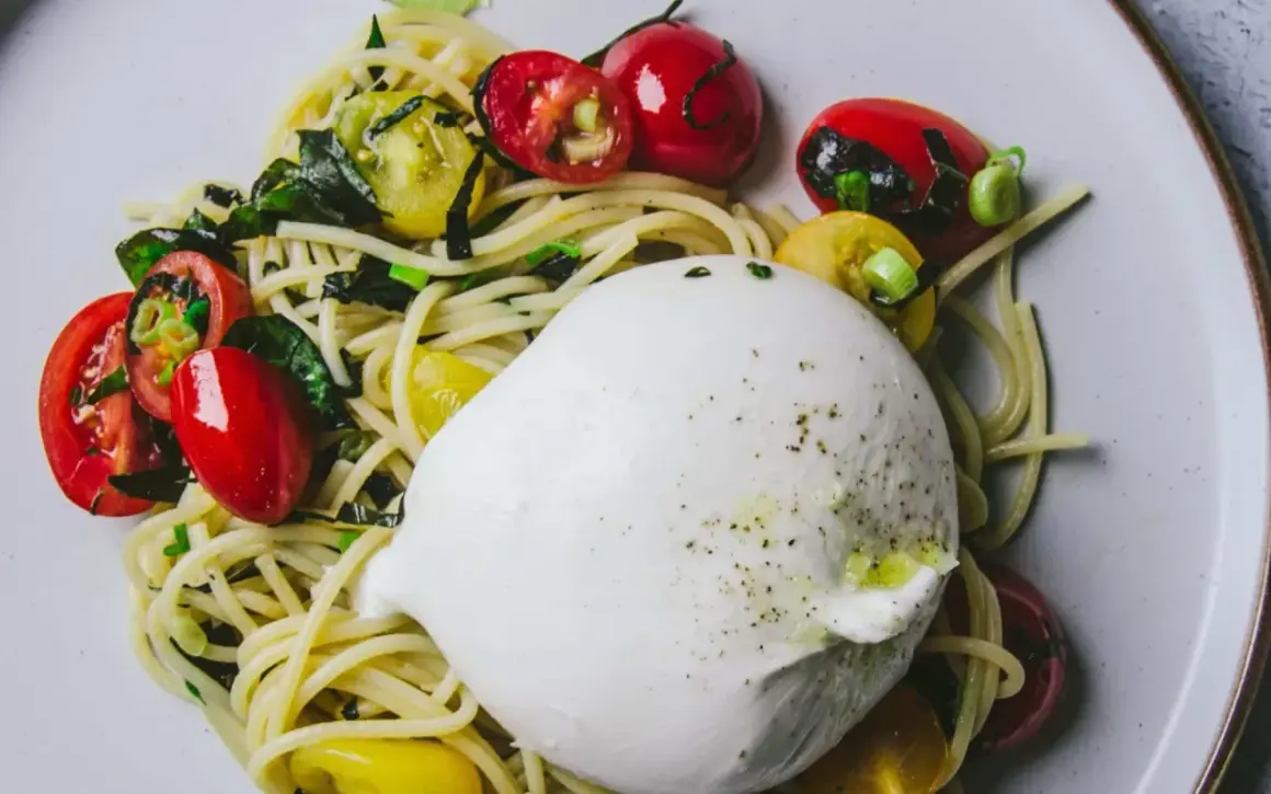 Un plat de pâtes avec une burrata crémeuse, des tomates cerises rouges et jaunes, et des herbes vertes.