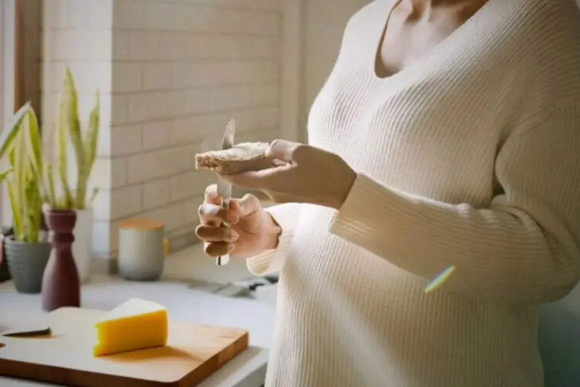 Une personne tartine une tranche de pain avec du fromage au lait cru. Un morceau de fromage est posé sur une planche à découper.