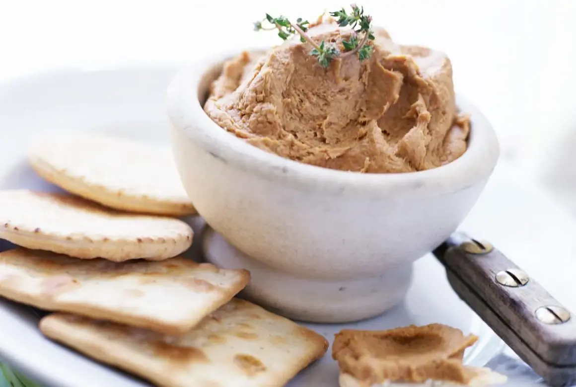 Un bol de pâté onctueux, garni de thym, servi avec des crackers. Un débat culinaire : foie gras vs pâté.