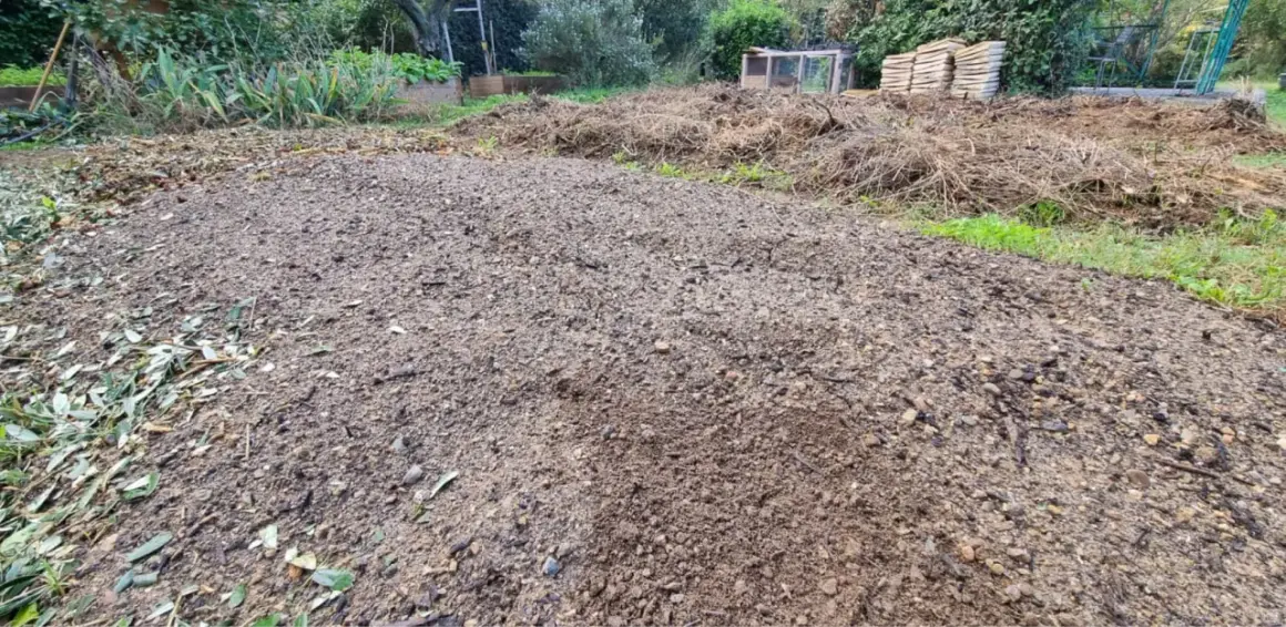 Vaste tas de terre dure comme de la pierre, prête pour le jardinage. Des débris végétaux et des feuilles jonchent le sol.