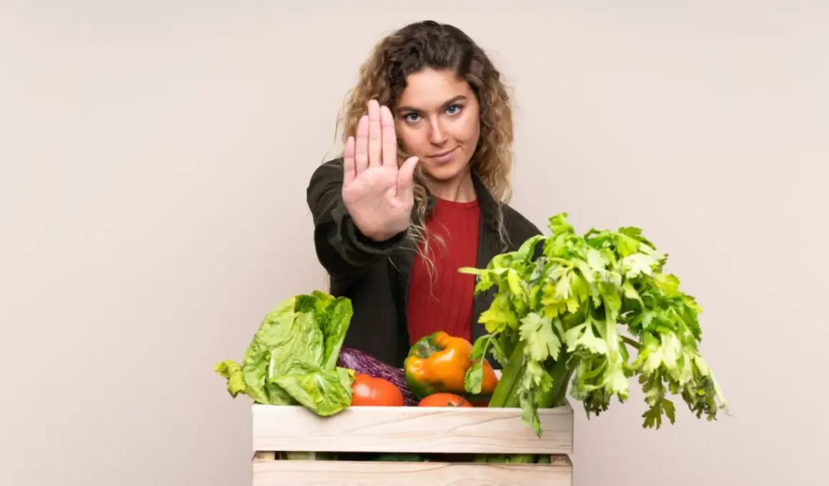 Femme faisant un geste d'arrêt devant une caisse de légumes frais, comme pour dire non aux légumes crus toxiques.