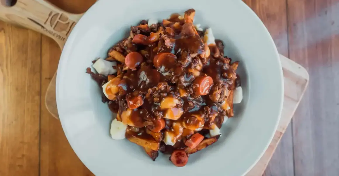 Une assiette généreuse de recette poutine québécoise, avec frites, fromage en grains, sauce brune et morceaux de saucisses.