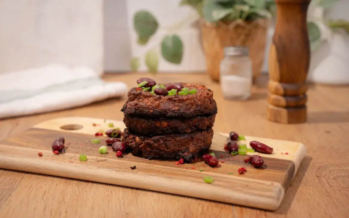 Trois galettes de haricot rouge empilées, garnies de haricots rouges et de ciboule. Épices et haricots rouges parsèment la planche à découper.