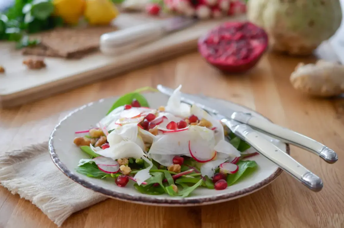 Salade croquante de céleri rave, radis, grenade et noix, garnie de feuilles vertes. Un délice frais et coloré.