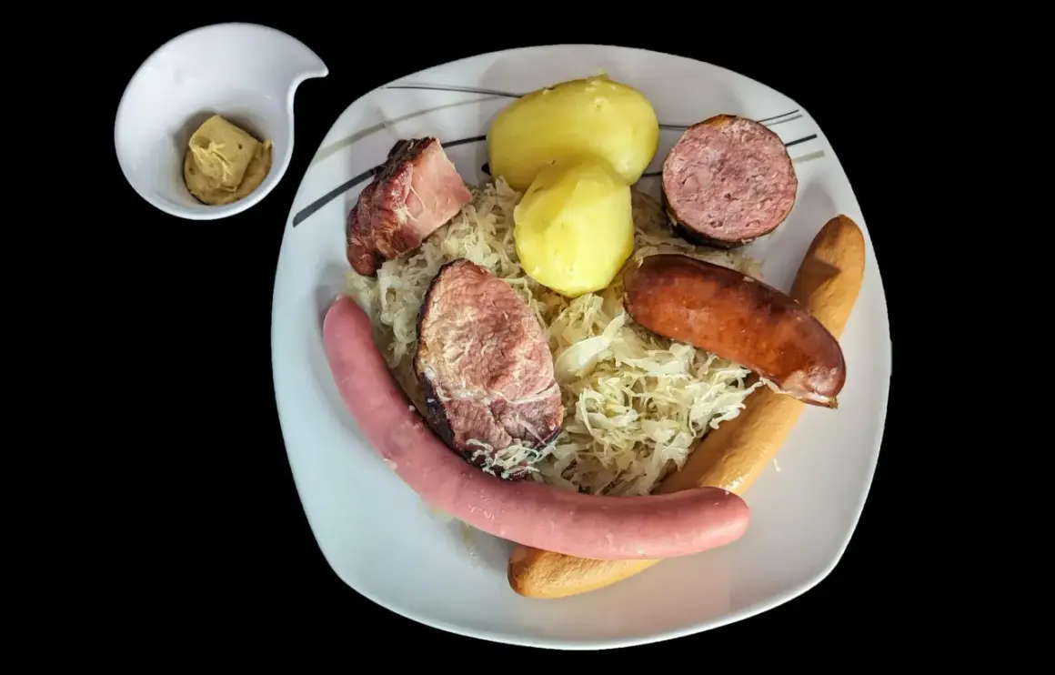 Assiette de choucroute garnie avec pommes de terre, saucisses et viandes, un petit ramequin de moutarde à côté. Un plat riche en saveurs et en vitamine C !