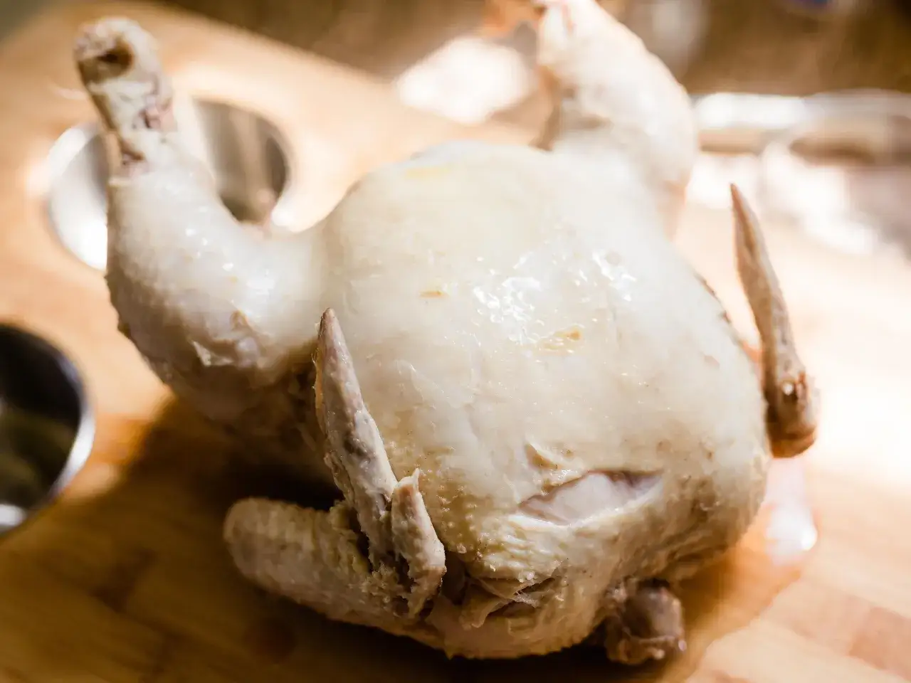 Un poulet entier, poch&eacute; dans un bouillon savoureux, repose sur une planche en bois. Sa peau est p&acirc;le et l&eacute;g&egrave;rement humide, pr&ecirc;te &agrave; &ecirc;tre d&eacute;gust&eacute;e.