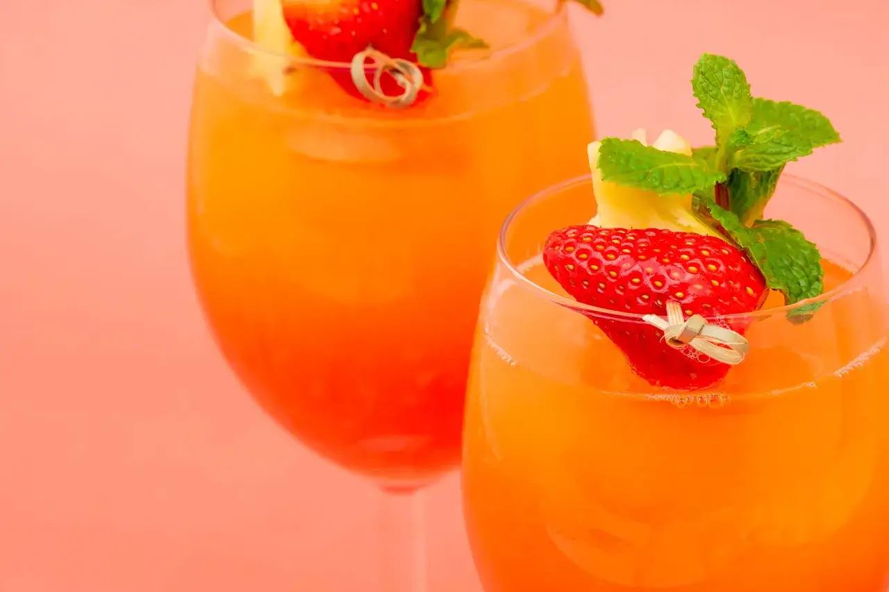Deux verres de mocktail orange vif, garnis de fraises, d'ananas et de menthe. Parfait pour savoir c'est quoi un mocktail.