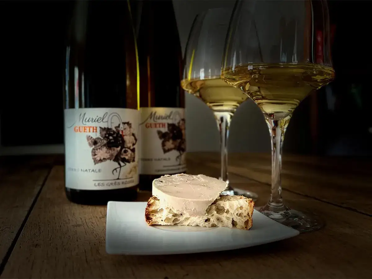 Quel vin d'Alsace servir avec du foie gras ? Deux verres de vin blanc, des bouteilles Muriel Gueth et une tranche de pain avec du foie gras.