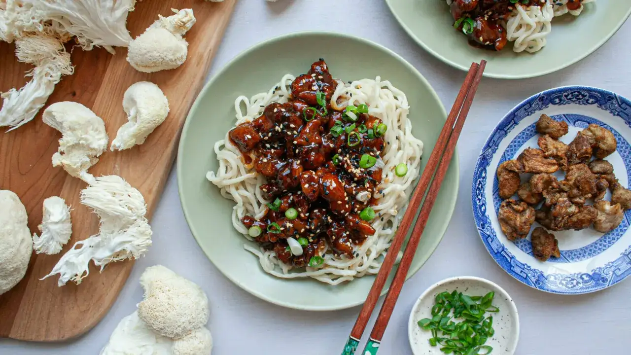 Champignons crini&egrave;re de lion crus et cuisin&eacute;s, servis avec des nouilles et une sauce brune.