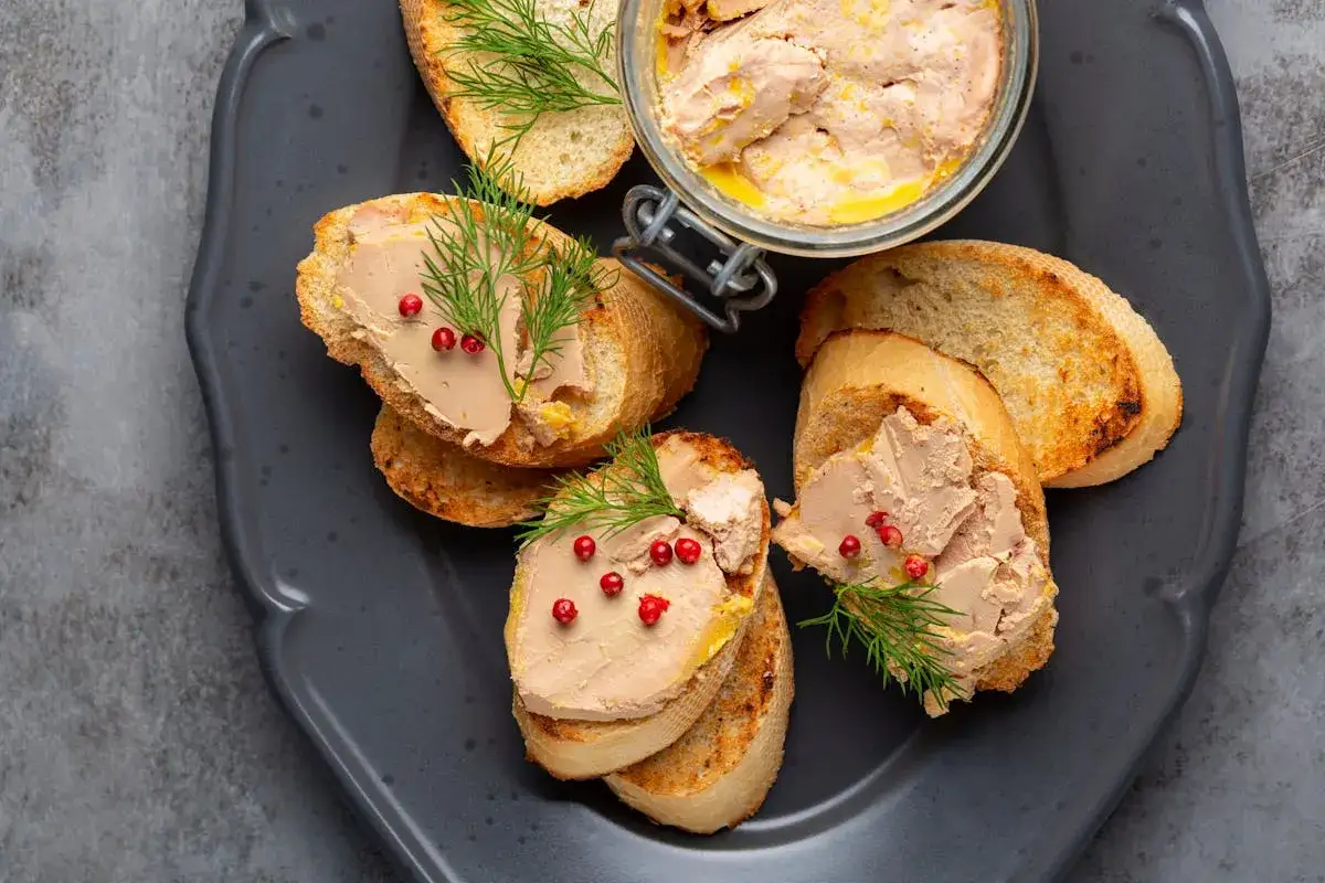 Toasts garnis avec du foie gras, des baies roses et de l'aneth. Un pot de foie gras est visible en arri&egrave;re-plan.