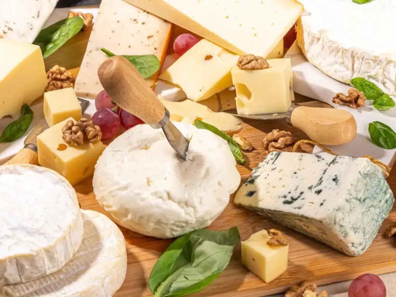 Un assortiment de fromages vari&eacute;s, dont un bleu persill&eacute;, un fromage frais et des cubes de fromage, avec des noix et des raisins. Un aper&ccedil;u du tableau calorique des fromages.