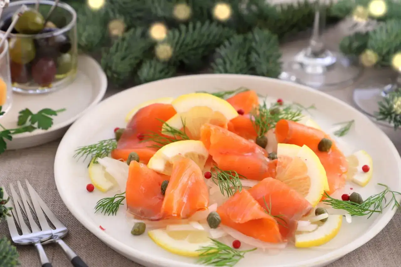 Belle pr&eacute;sentation de saumon fum&eacute; sur une assiette, d&eacute;cor&eacute;e de citrons, c&acirc;pres et aneth. Parfait pour un No&euml;l festif.