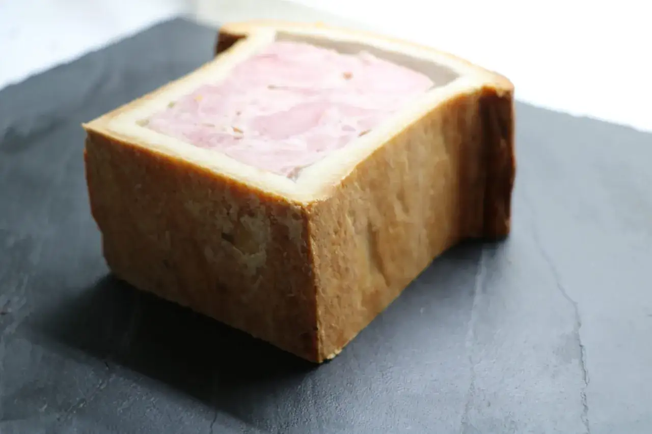 Un bloc de p&acirc;t&eacute; en cro&ucirc;te, garni de viande rose, repose sur une surface sombre.