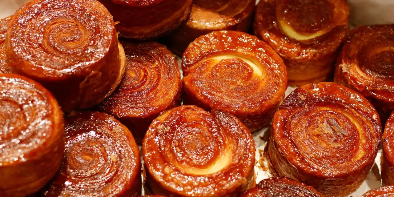Gros plan sur des kouign amann brillants, leur signification r&eacute;side dans leur caramel croustillant et leur p&acirc;te feuillet&eacute;e.