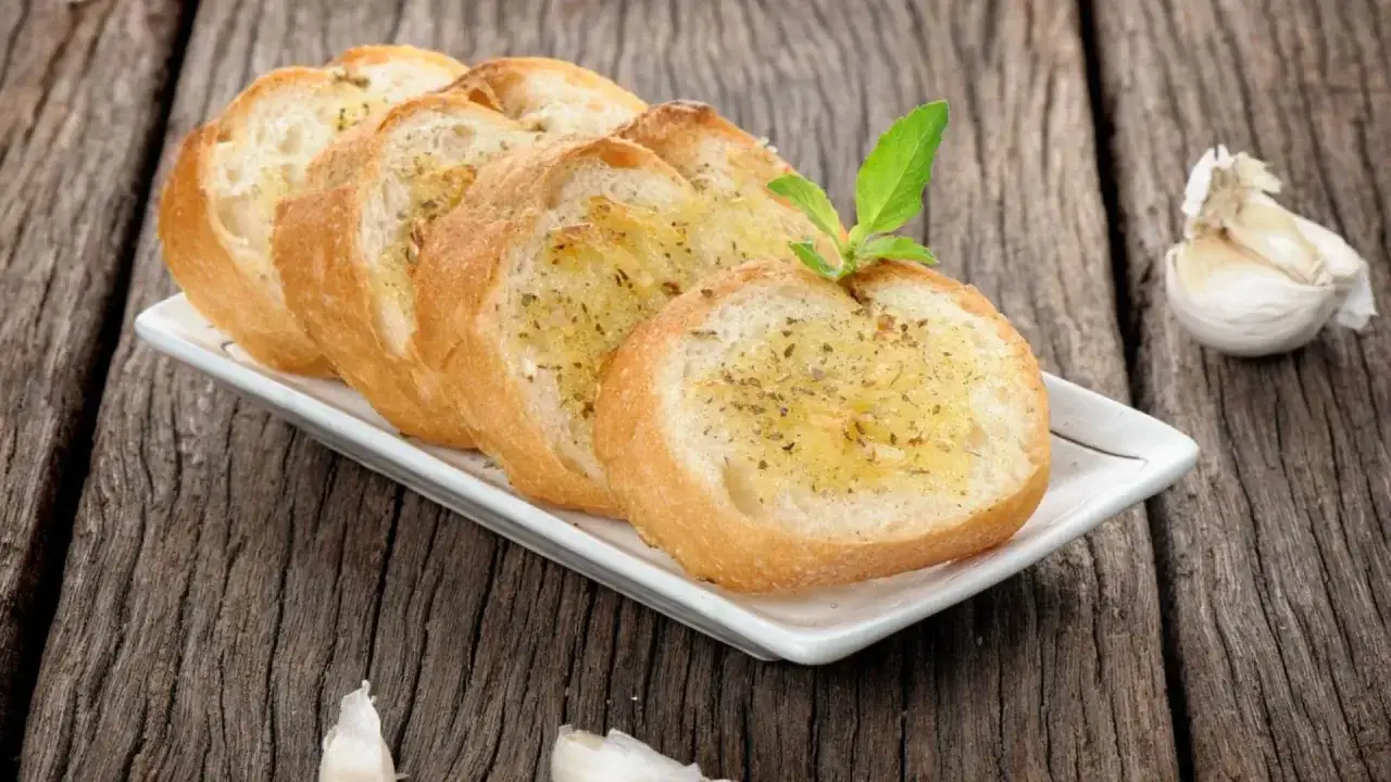 Tranches de pain grill&eacute; &agrave; l'ail, garnies d'herbes, rappelant la pr&eacute;fou recette traditionnelle. Une t&ecirc;te d'ail repose &agrave; c&ocirc;t&eacute;.