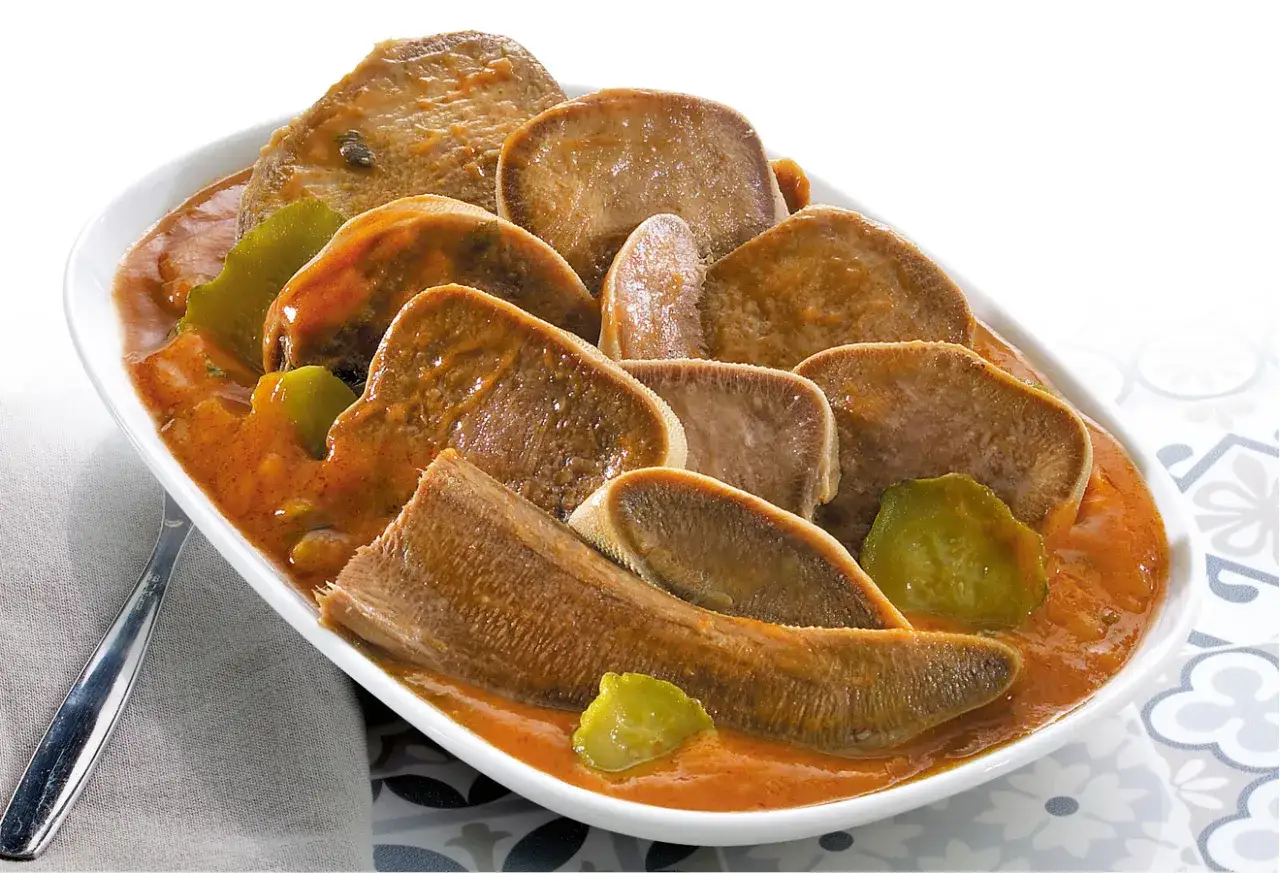 Plat de langue de boeuf en sauce, une recette savoureuse et r&eacute;confortante. Les tranches de langue sont tendres et napp&eacute;es d'une sauce orang&eacute;e, accompagn&eacute;es de quelques morceaux de l&eacute;gumes verts.