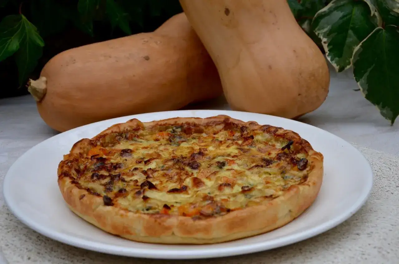 Une délicieuse tarte à la courge dorée, prête à être dégustée, avec deux courges butternut en arrière-plan.
