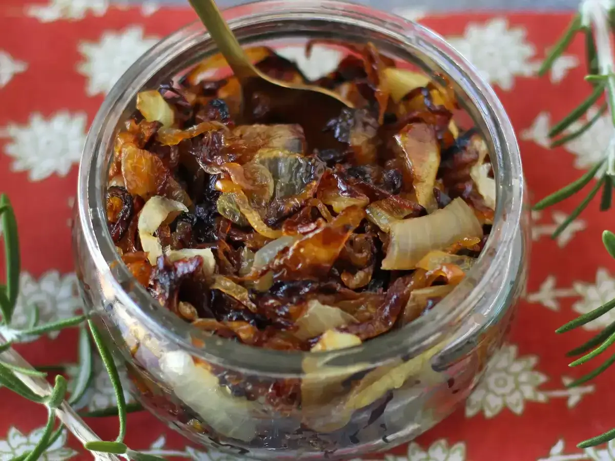 Un pot de confit d'oignons caram&eacute;lis&eacute;s, parfait pour savoir comment faire un confit d'oignons maison. Une cuill&egrave;re dor&eacute;e y est plong&eacute;e.