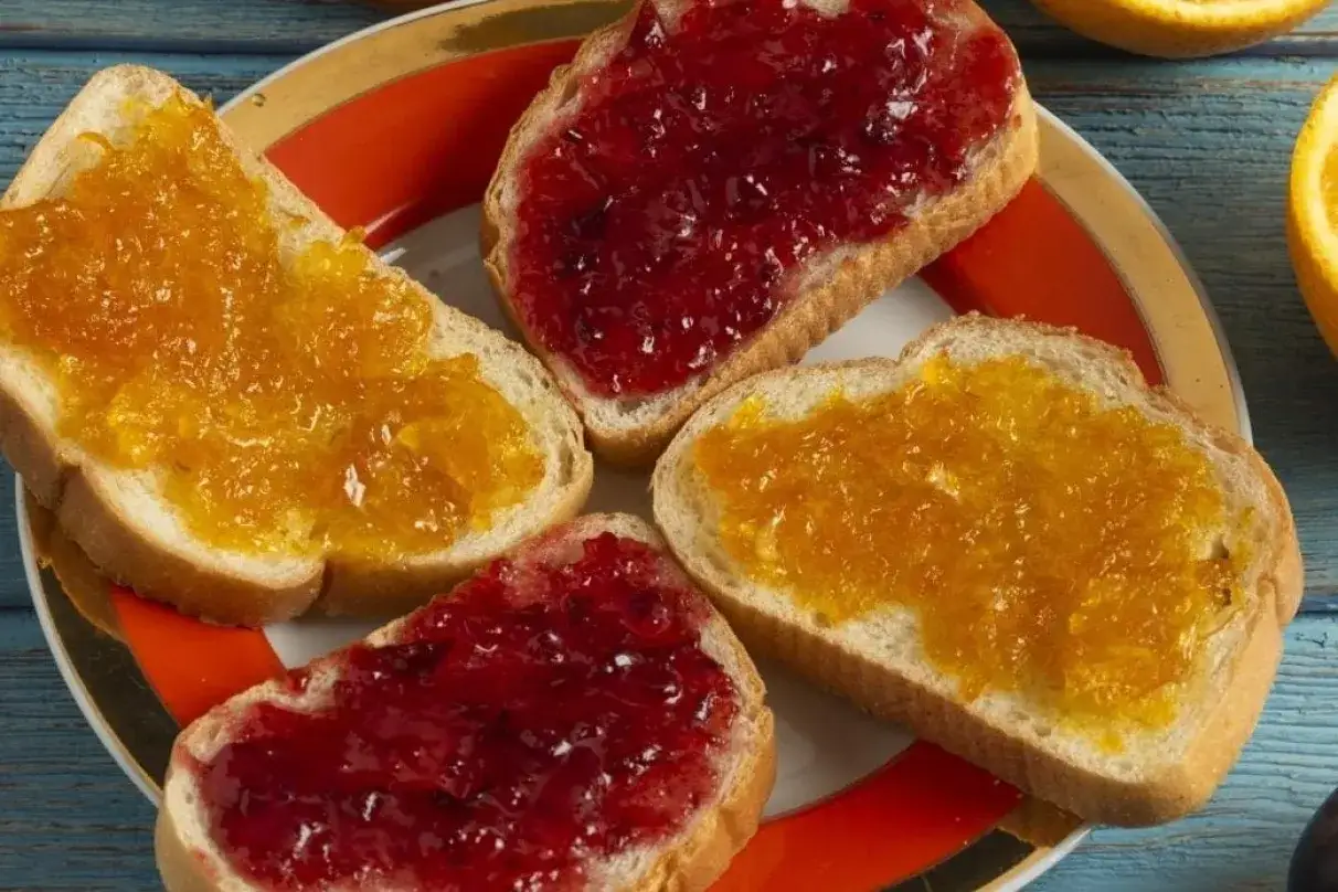 Quatre tranches de pain de mie garnies de marmelade orange et de confiture rouge. La diff&eacute;rence entre marmelade et confiture est visible.