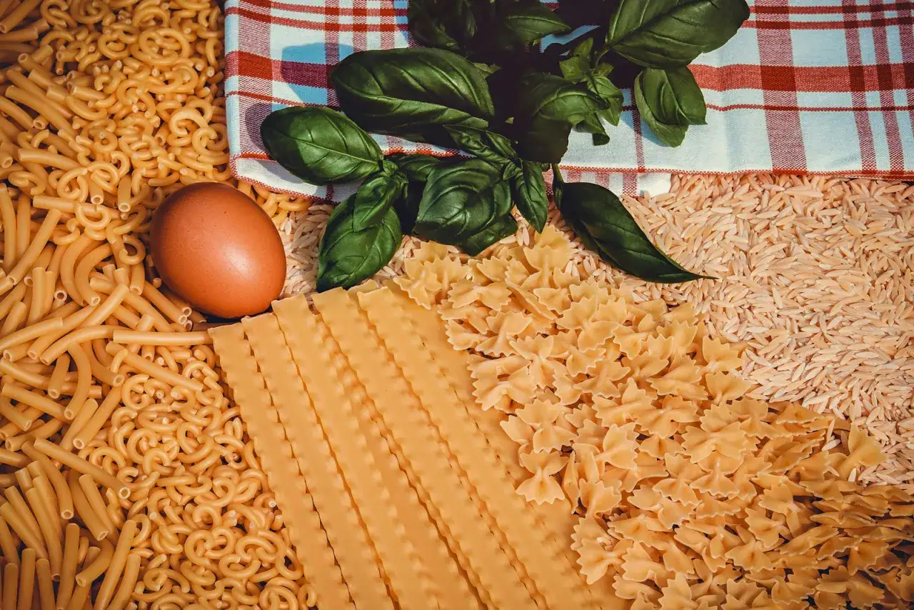 Assortiment de pâtes, riz, œuf et basilic. Ces aliments, riches en gluten, invitent à un festin italien.